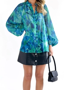 Détail de chemisier en mousseline bleue avec jupe en cuir noir et sac à main assorti