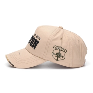 Detail of khaki baseball cap featuring 3D embroidery and distressed ripped brim edge