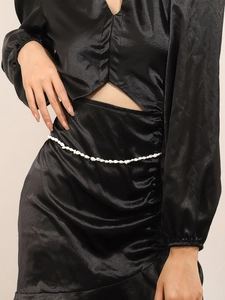 Detail of white beaded shell waist chain styled over a black satin dress for beach vacation