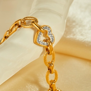 Macro shot of gold twisted chain bracelet featuring a white heart pendant with zircons