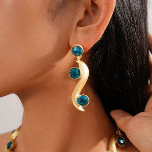 Close-up of golden S-shaped drop earrings with three faceted blue crystals on model
