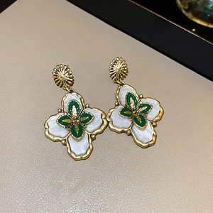 Détail macro de boucles d'oreilles vintage avec croix en émail vert et pétales blancs