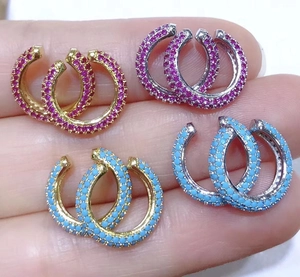 Close-up of C-shaped ear cuffs with pink and blue stones in gold and silver finish
