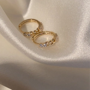 Detailed macro view of gold chain link huggie earrings with cubic zirconia on silk