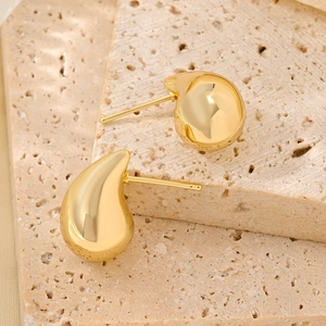 Macro shot of 14K gold-plated teardrop earrings on natural beige stone texture