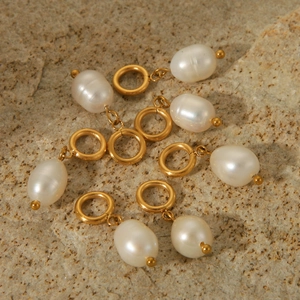 Set of seven white baroque pearl pendants with gold-plated metal loops on stone surface