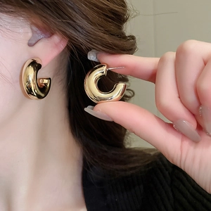 Detail of golden chunky C-shaped hoop earrings with smooth metallic finish on model