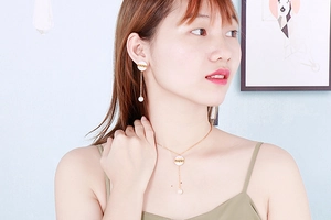 Close-up of golden LOVE pendant necklace and pearl earrings on a model with soft lighting