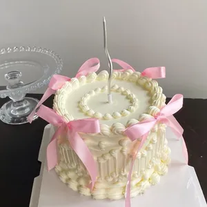 Détail du gâteau à la crème avec nœuds en satin rose et bougie argentée ondulée