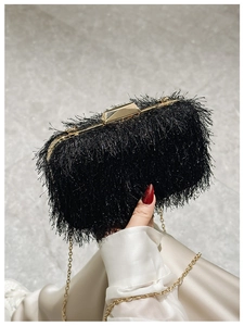 Detail of black fringe evening clutch bag with gold metal hardware and chain strap