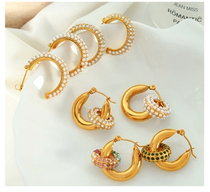Close-up of gold-plated titanium steel hoop earrings with pearls and crystals on white dish