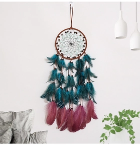 Detailed view of handmade dream catcher with teal and purple feathers on white wall