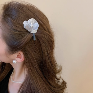 Gros plan d'une pince à cheveux fleur marbrée avec perle sur cheveux bruns