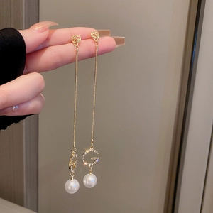 Detail of long gold tassel earring with sparkling rhinestones, letter G and white pearl