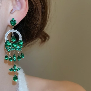 Close-up of long tassel earrings featuring green heart and teardrop shaped gemstones
