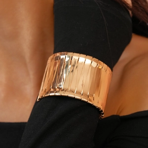 Close-up of a wide irregular gold cuff bracelet worn over a stylish black sleeve