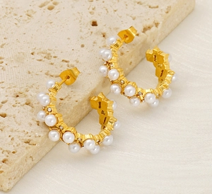 Detail of C-shaped gold pearl earrings with crystals on textured travertine stone