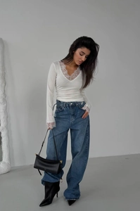 Detail of white lace V-neck long sleeve top styled with high-waisted blue denim jeans