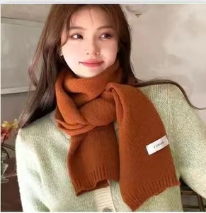 Detail of caramel knitted scarf with a minimalist white woven brand label