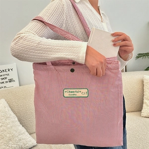 Detail of red checkered canvas tote bag with embroidered patch and metal buckle closure