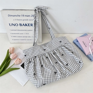 Detail of checkered canvas tote bag featuring black bow embroidery and ribbon straps
