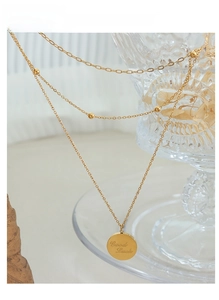 Detail of double-layer gold necklace with small beads and Good Luck engraved round pendant