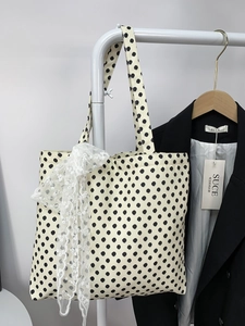 Close-up of beige polka dot canvas tote bag featuring a large white lace bow detail