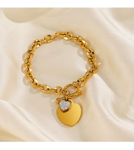 Détail d'un bracelet doré avec fermoir OT, cœur poli et breloque cœur ornée de cristaux