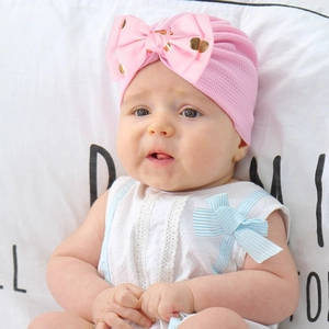 Baby girl pink turban hat with large gold polka dot bow shown on a cute infant model