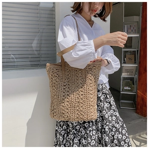 Detail of hollow woven straw tote bag with brown leather handles on shoulder