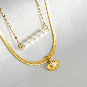 Detail of gold ginkgo leaf pendant and pearl layered necklace on silk fabric background