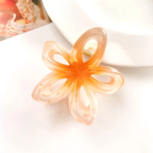 Detail of orange gradient frangipani hair claw clip on a white ceramic plate