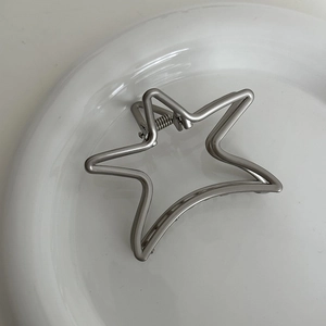 Macro shot of silver star-shaped metal hair claw clip on a minimalist ceramic plate