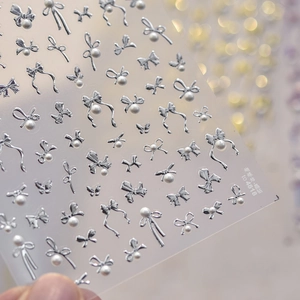 Close-up of 3D silver bow nail stickers with white pearls on transparent backing