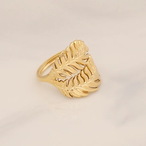 Macro shot of gold leaf-shaped hollowed metal ring on a white marble background
