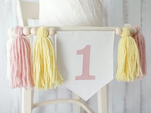 Detail of pink and yellow yarn tassels with wood beads on a birthday highchair banner