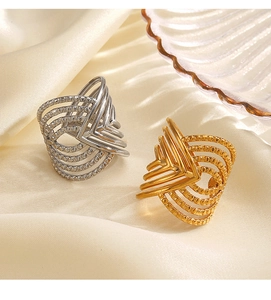 Detailed view of gold and silver crossover geometric rings on elegant beige satin fabric