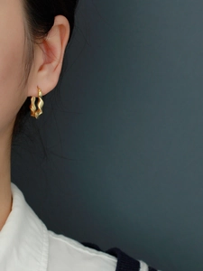 Macro detail of a wavy gold hoop earring on a model with premium metallic texture
