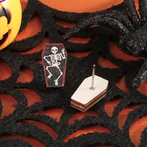 Detailed close-up of coffin-shaped wooden stud earrings with a skull pattern on a spider web