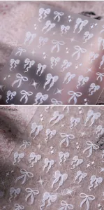 Macro detail of 5D embossed white ribbon bow and star nail art stickers on transparent film
