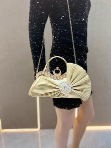 Detailed view of a gold pleated evening clutch with crystal buckle on a black sequin dress