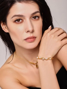 Close-up of wavy gold bangle with pearls and matching necklace on a model