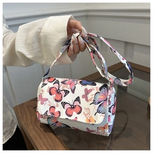 Detail of a beige handbag with colorful butterfly prints and matching shoulder strap