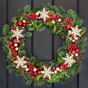Christmas wreath with green pine needles, red berries, gold ornaments on black wood background