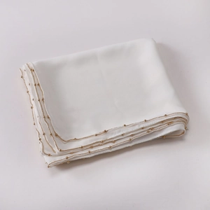 Detail view of smooth white silk fabric with luxury golden beaded chain trim edges