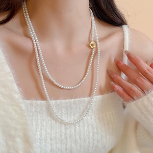 Detail of layered white pearl necklace with golden flower toggle clasp on model