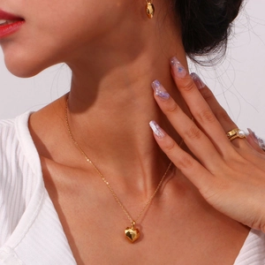 Macro detail of gold heart pendant necklace with pearl ring and earring on model