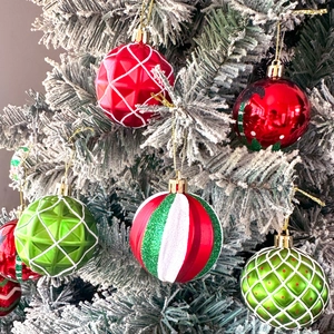 Close-up of glittery red and green Christmas ornaments hanging on a snowy cedar tree