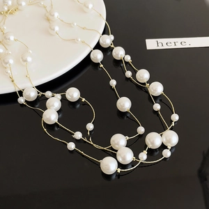 Detail of layered gold-tone necklace with multi-sized white pearls on reflective surface