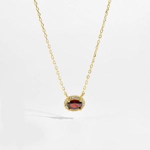 Macro shot of red oval gemstone pendant surrounded by white zircon on a gold necklace